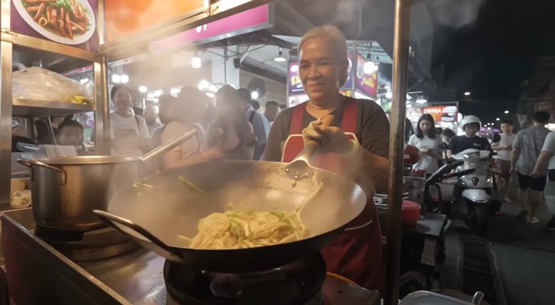 FLUX 3: una cuoca di strada salta i noodles nel wok in una strada notturna all'aperto, con folla e scooter alle sue spalle